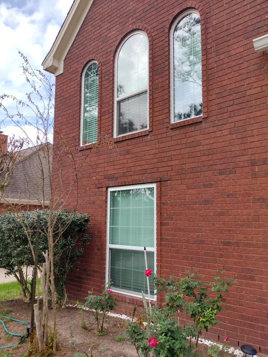 custom arched windows and rectangular window on side of brick home above rose garden